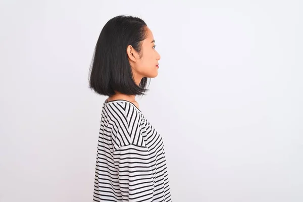 年轻的中国女人穿着条纹T恤 站在孤独的白色背景上 望着旁边 带着自信的微笑放松自己的姿态 — 图库照片