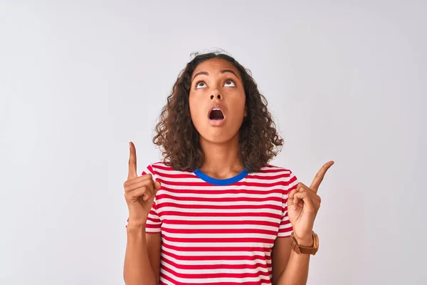 年轻的巴西女人穿着红色条纹T恤 站在孤立的白色背景上 惊讶地抬起头 用手指和胳膊指指着 — 图库照片