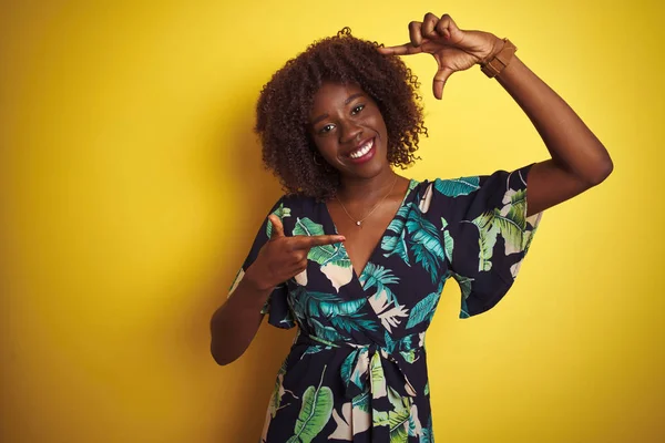 孤立した黄色の背景に夏の花のドレスを着た若いアフリカのアフロ女性は 幸せな顔をした手と指でフレームを作り笑顔 創造性と写真の概念 — ストック写真