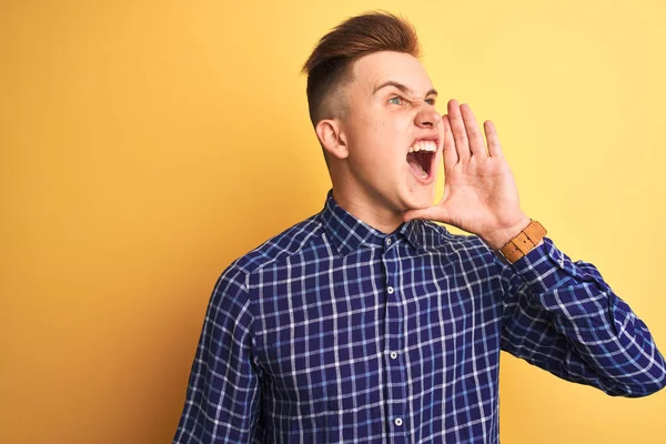 Sarı arka planda dikilip el ele tutuşarak bağıran genç ve yakışıklı bir adam. İletişim konsepti.