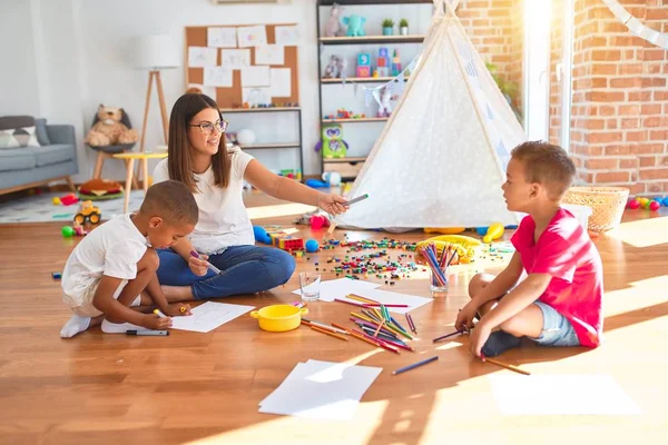 Genç ve güzel öğretmenler yerde oturup anaokulunda bir sürü oyuncak çiziyorlar.