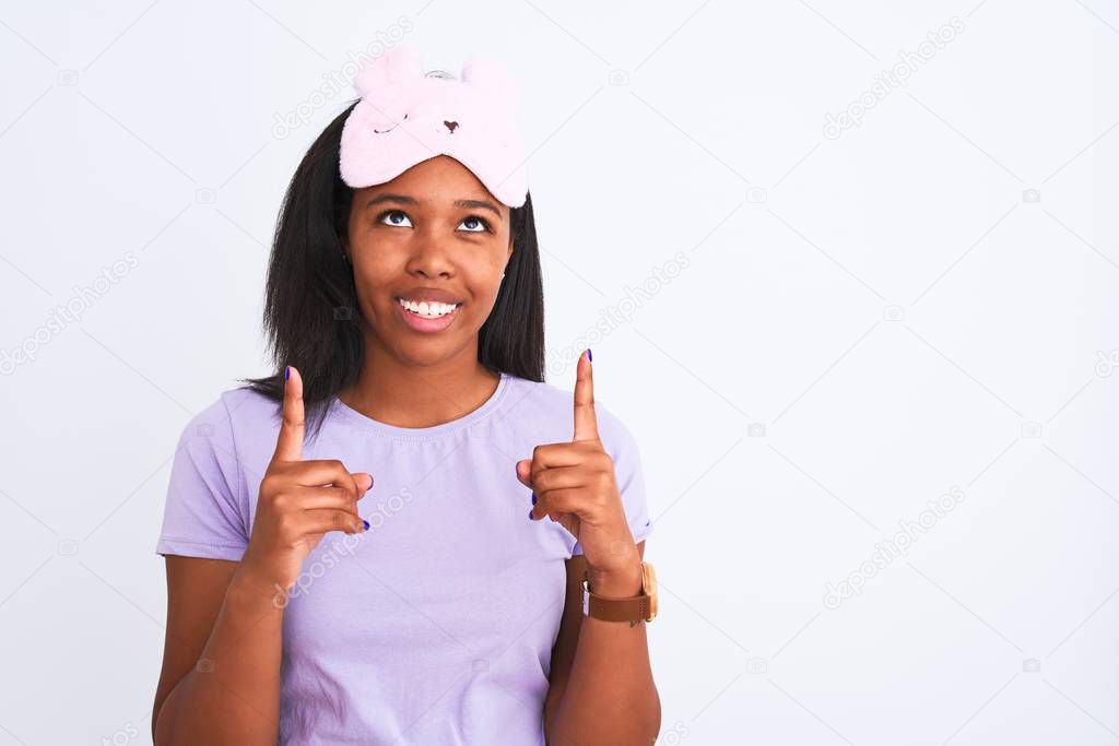 Young african american woman wearing sleeping mask over isolated background amazed and surprised looking up and pointing with fingers and raised arms.