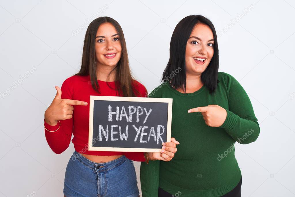 Beautiful women holding blackboard happy new year message over isolated white background very happy pointing with hand and finger