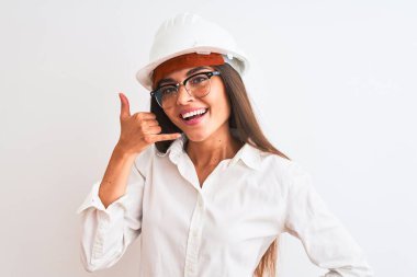 Kask ve gözlük takan genç, güzel mimar kadın izole edilmiş beyaz arka planda gülümsüyor telefonla el ve parmaklarıyla telefonla konuşuyor gibi yapıyor. İletişim kavramları.