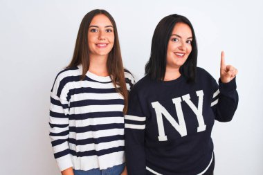 İzole edilmiş beyaz arka planda dikilen gündelik giysiler giyen genç ve güzel kadınlar bir numaralı parmağı gösterirken kendinden emin ve mutlu bir şekilde gülümsüyorlar..