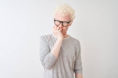 İzole edilmiş beyaz arka plan üzerinde çizgili tişört ve gözlük takan genç albino sarışın adam elleri ağız yiyen tırnaklarla stresli ve gergin görünüyor. Endişe sorunu.
