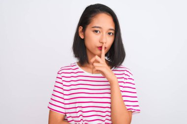 İzole edilmiş beyaz arka planda duran çizgili tişört giyen genç Çinli kadın sessiz olmak istiyor. Sessizlik ve gizli konsept.
