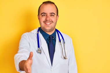 Ceket ve steteskop giyen genç doktor izole edilmiş sarı arka planda durup dostça gülümseyerek selamlama ve hoş geldin diyor. Başarılı bir iş..