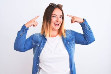 İzole edilmiş beyaz arka planda duran kot gömlekli güzel bir kadın iki eliyle başını gösteren bir gülümseme, harika bir fikir ya da düşünce, iyi bir hafıza