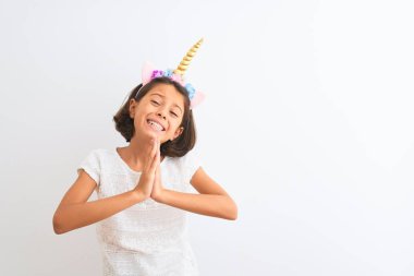 Tek boynuzlu at diademi giymiş güzel bir kız çocuğu izole edilmiş beyaz arka planda duruyor. Elleri bağlı yalvarıyor ve dua ediyor. Yüzünde umut ifadesi var. Af diliyor. Din kavramı.