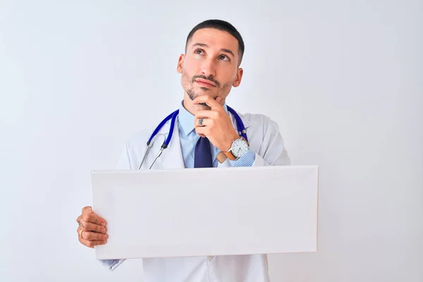 孤立した背景深刻な顔の上に空白の広告バナーを持っている若い医師の男質問について考えて 非常に混乱したアイデア — ストック写真