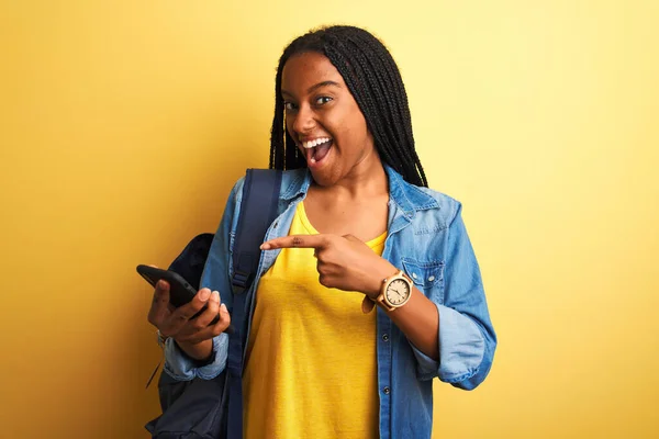 African american student woman using smartphone standing over isolated yellow background very happy pointing with hand and finger