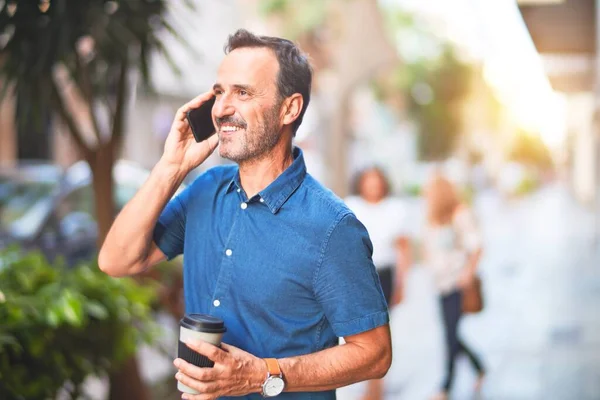 中年英俊的商人站在街上用智能手机聊天 一边喝着咖啡 一边笑着把咖啡带走 — 图库照片