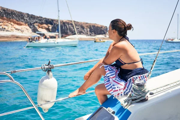 Genç ve güzel bir kadın mutlu bir şekilde gülümsüyor, güneşli bir günde teknede yelken açıyor.