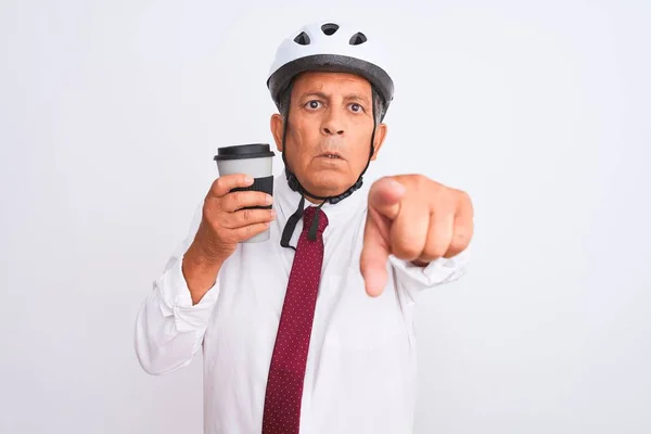 Senior businessman wearing bike helmet drinking coffee over isolated white background pointing with finger to the camera and to you, hand sign, positive and confident gesture from the front