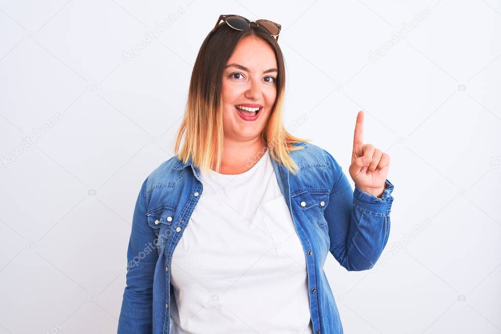 Beautiful woman wearing denim shirt standing over isolated white background showing and pointing up with finger number one while smiling confident and happy.