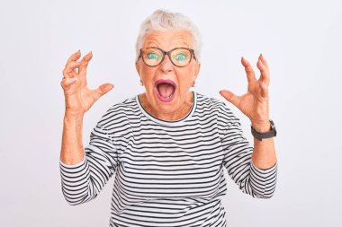 Üst düzey gri saçlı kadın izole edilmiş beyaz arka plan üzerine çizgili donanma tişörtü gözlüğü takıyor deli gibi bağırıyor ve agresif bir ifade ve kolla bağırıyor. Hayal kırıklığı konsepti.