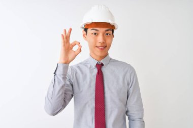 Kravat ve kask takan Çinli mimar izole edilmiş beyaz arka planda durup gülümsüyor ve el ve parmaklarıyla 
