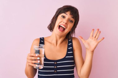 Genç, güzel bir kadın pembe arka planda duran bir bardak su tutuyor. Mutlu ve heyecanlı. Kazanan ifade zaferi büyük bir gülümsemeyle kutluyor ve ellerini kaldırıyor.