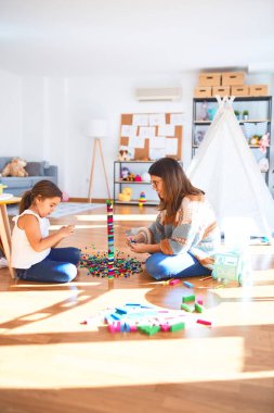 Güzel öğretmen ve bebek anaokulunda oyuncakların etrafında yapı taşlarıyla oynuyorlar.