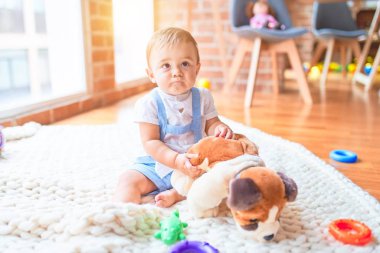 Güzel çocuk, anaokulunda battaniyeye oturmuş oyuncak köpekle oynuyor.