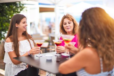 Güzel bir grup kadın restoranın terasında oturmuş kokteyller içiyor konuşuyor ve gülümsüyor.