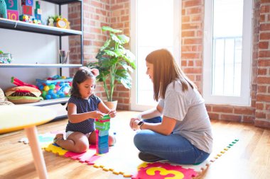 Güzel öğretmen ve küçük kız anaokulunda inşaat bloklarıyla oynuyorlar.