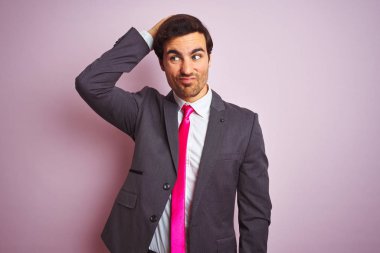 Takım elbiseli ve kravatlı genç yakışıklı iş adamı soyutlanmış pembe arka planda duruyor. Soruları merak ediyor. Şüpheyle kararsız, kafa kafaya düşünerek. Düşünceli kavram.