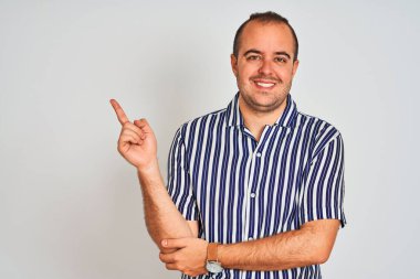 Mavi çizgili gömlekli genç adam izole edilmiş beyaz arka planda duruyor. Yüzünde kocaman bir gülümseme var. Eli ve parmağı kameraya bakıyor..
