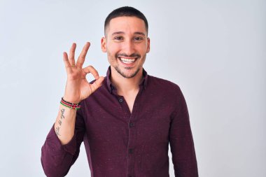 Genç yakışıklı iş adamı izole edilmiş arka planda durup gülümsüyor ve el ve parmaklarıyla 