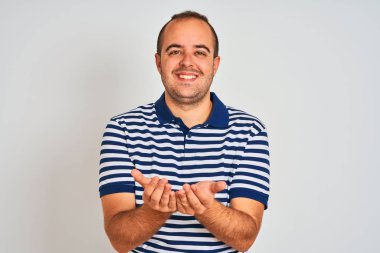 Sıradan çizgili polo giyen genç adam izole edilmiş beyaz arka planda durup avuçlarını birbirine değdirirken ya da hareket ederken gülümsüyor. Tutun ve koruyun