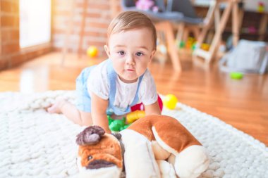 Güzel çocuk, anaokulunda battaniyeye oturmuş oyuncak köpekle oynuyor.