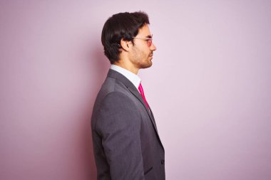 Genç yakışıklı iş adamı takım elbise ve güneş gözlüğü takıyor. Pembe arka planda. Taraf arıyor, rahat profil pozu veriyor..