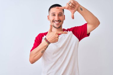 İzole edilmiş arka planda duran yakışıklı genç adam gülümsüyor ve elleri ve parmakları gülen yüzlü bir çerçeve yapıyor. Yaratıcılık ve fotoğrafçılık kavramı.