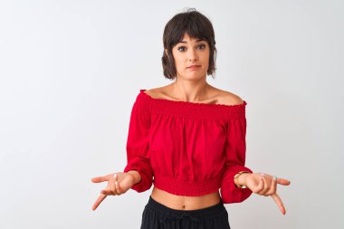 Kırmızı yaz tişörtü giyen genç ve güzel bir kadın izole edilmiş beyaz arka planda duruyor ve kolları açık, hiçbir fikri yok..