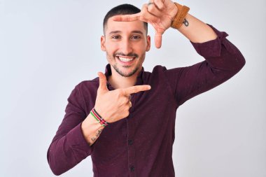 Genç yakışıklı iş adamı izole edilmiş arka planda duruyor gülümsüyor ve elleri ve parmakları gülen yüzlü bir çerçeve yapıyor. Yaratıcılık ve fotoğrafçılık kavramı.