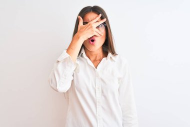 Gözlüklü genç ve güzel bir iş kadını izole edilmiş beyaz arka planda dikiliyor. Şoka giriyor, yüzünü ve gözlerini eliyle kapatıyor, utangaç ifadesiyle parmaklarından bakıyor..