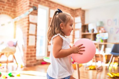 Genç, güzel sarışın kız anaokulunda oyuncaklarla oyun oynuyor, gülümsüyor, evde balyalarla oynuyor.
