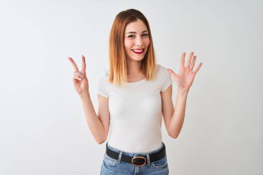Güzel kızıl saçlı kadın rahat t-shirt izole beyaz arka plan üzerinde duran gösteren ve parmakları ile işaret ederken emin ve mutlu gülümseyerek yedi numara.