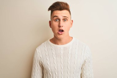 Kışlık süveter giyen yakışıklı genç adam izole edilmiş beyaz arka planda korku ve şaşkınlık dolu bir ifadeyle duruyor..