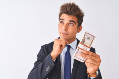 Soyutlanmış beyaz arka planda dolar tutan takım elbiseli yakışıklı bir işadamı. Ciddi bir yüz. Soru soran, kafası karışık bir fikir.