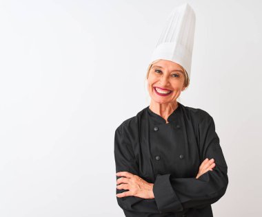 Üniformalı ve şapkalı orta yaşlı aşçı kadın izole edilmiş beyaz arka planda duruyor. Kollarını kavuşturup kameraya bakarken gülümsüyor. Pozitif kişi.