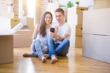 Karton kutuların etrafında akıllı telefon kullanan güzel bir çift gururla bağırıyor ve zaferi ve başarıyı kutluyor. Çok heyecanlı, coşkulu bir duygu.