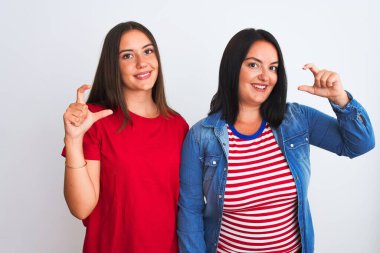 İzole edilmiş beyaz arka planda dikilen rahat kıyafetler giyen genç ve güzel kadınlar gülümsüyor ve el hareketleriyle küçük beden işareti yaparak kameraya bakıyorlar. Ölçü kavramı.