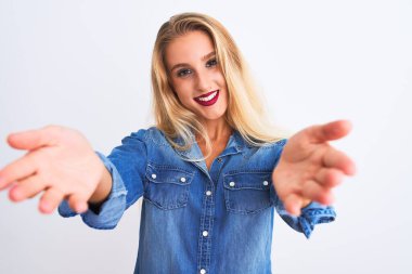 İzole edilmiş beyaz arka plan üzerinde duran sıradan bir kot gömlek giyen genç ve güzel bir kadın neşeli bir şekilde el ele tutuşup kabul görüyor..