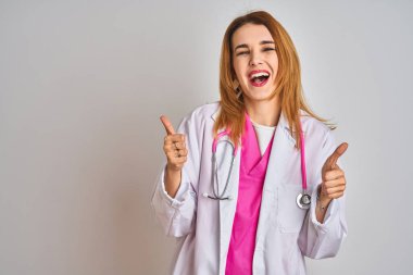 Kızıl saçlı beyaz kadın pembe steteskop takmış arka plan başarı tabelasına el hareketleriyle olumlu jest yapıyor, gülümsüyor ve mutlu. Neşeli ifade ve kazanan jest.