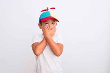 Güzel bir çocuk, pervaneli, kuku renkli bir şapka takmış beyaz arka planda ağzı yanlışlıkla ellerle kapatırken şok olmuş. Gizli konsept.