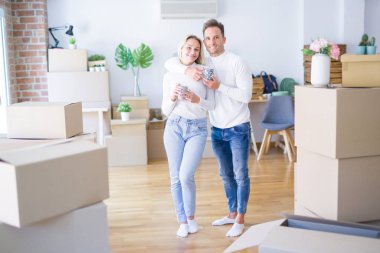 Genç güzel çift karton kutular etrafında yeni evde kahve fincan içme ayakta