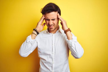 Zarif bir gömlek giyen genç yakışıklı iş adamı, izole edilmiş sarı arka planda duruyor. Başında ağrı var çünkü stres var. Migren ağrısı..