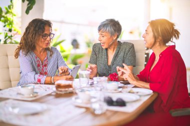 Orta yaşlı kadınlarla buluşup, öğle yemeği yiyip, kahve içiyorlar. Olgun arkadaşlar mutlu bir şekilde gülümsüyor. Güneşli bir günde evde akıllı telefon kullanıyorlar.